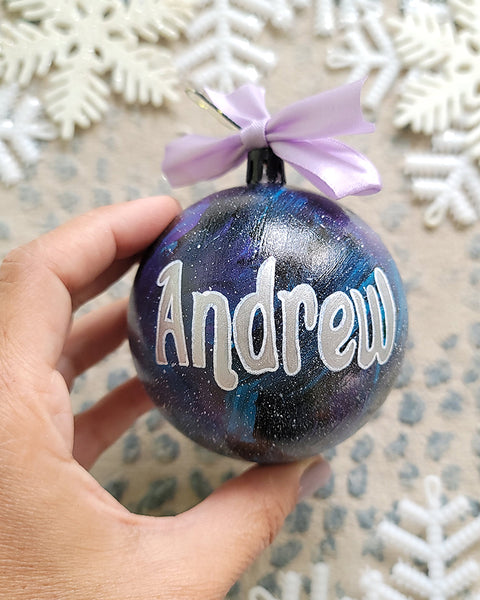 A Black galaxy hand painted ball ornament with the name "Andrew" in silver