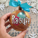 A Colorful hand painted ornament with choco brown background and colors of choco brown, indian pink, mint green and gold scattered all over with white dots and the name 