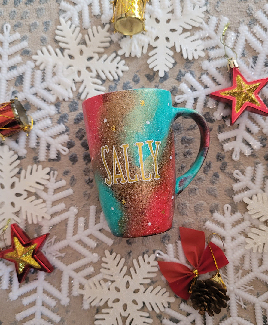 A Christmas galaxy colored hand painted mug with the name "sally" written gold with white dots and gold stars scattered all over