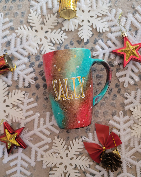 A Christmas galaxy colored hand painted mug with the name "sally" written gold with white dots and gold stars scattered all over