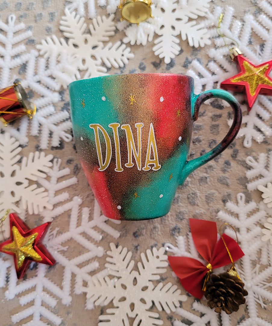 A Christmas hand painted mug with the name "Dina" written in gold