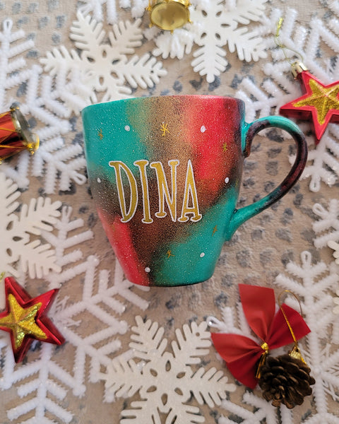 A Christmas hand painted mug with the name "Dina" written in gold