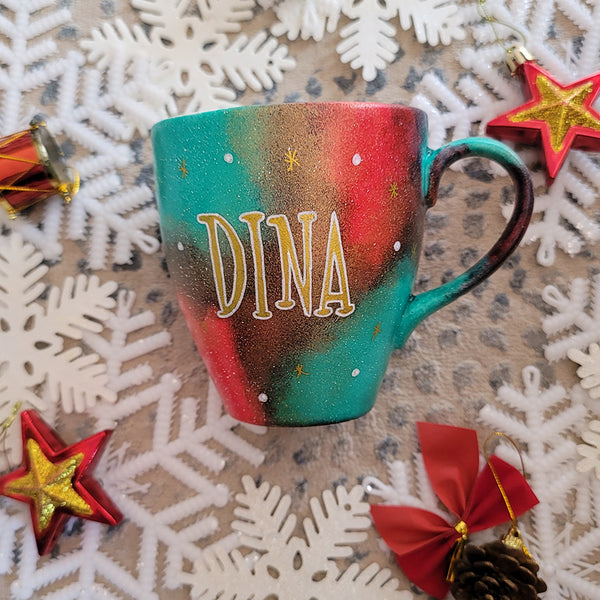 A Christmas hand painted mug with the name "Dina" written in gold