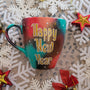 A Christmas galaxy colored hand painted mug with the words "Happy new year" written in gold and white dots and gold stars scattered all over