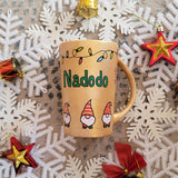 A Gold hand painted mug with gnomes all around the bottom half of the mug and festive lighting all over the top of the mug and the name nadodo in the center