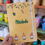 A Gold hand painted A5 Notebook with gnomes on the bottom and festive light on the top and the name 