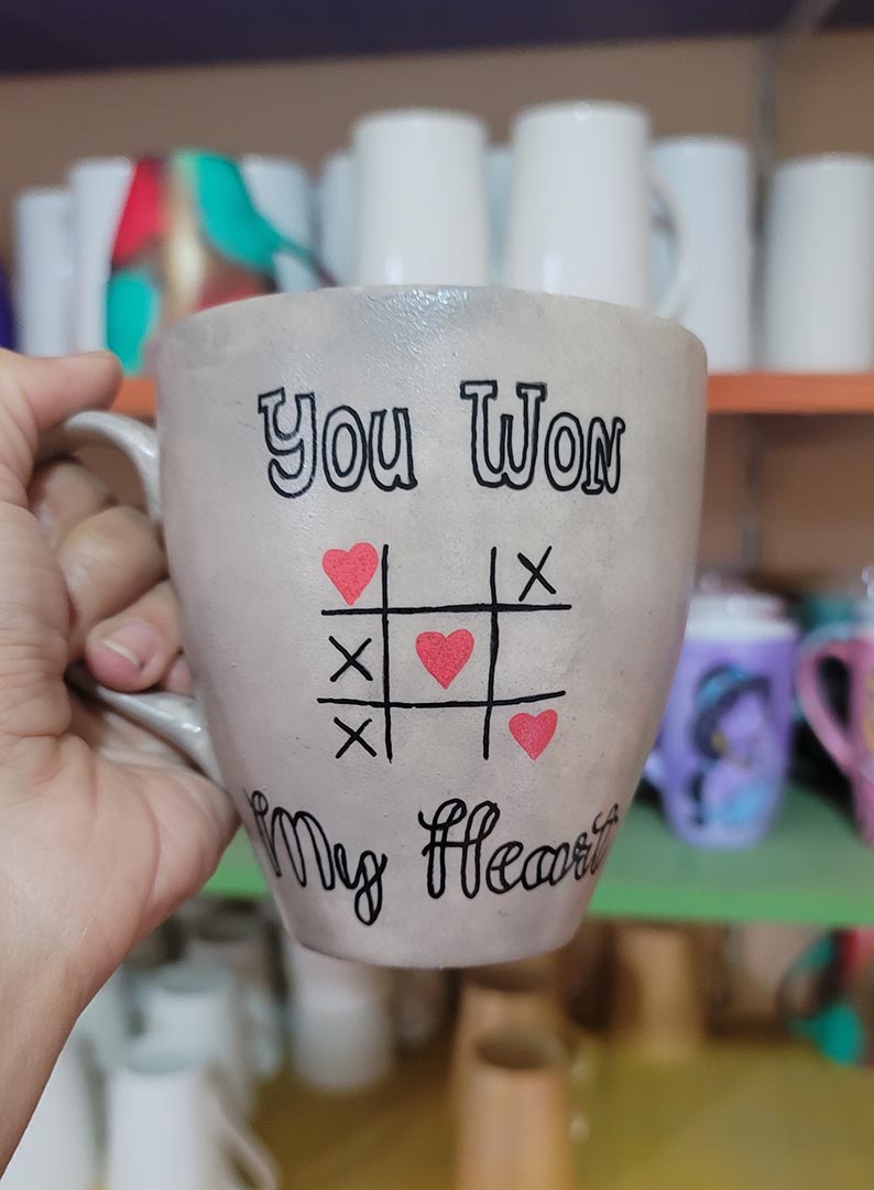 A hand painted Taupe mug with the sentence "you won" and under it an x o chart with hearts instead of o  and three hearts winning the game diagonally, then under it the words "My heart"