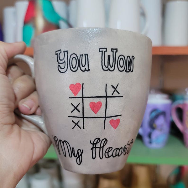 A hand painted Taupe mug with the sentence "you won" and under it an x o chart with hearts instead of o  and three hearts winning the game diagonally, then under it the words "My heart"