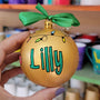 A gold hand painted ball ornament with festive lights all around the top and the name "Lilly" written in green outlined with black