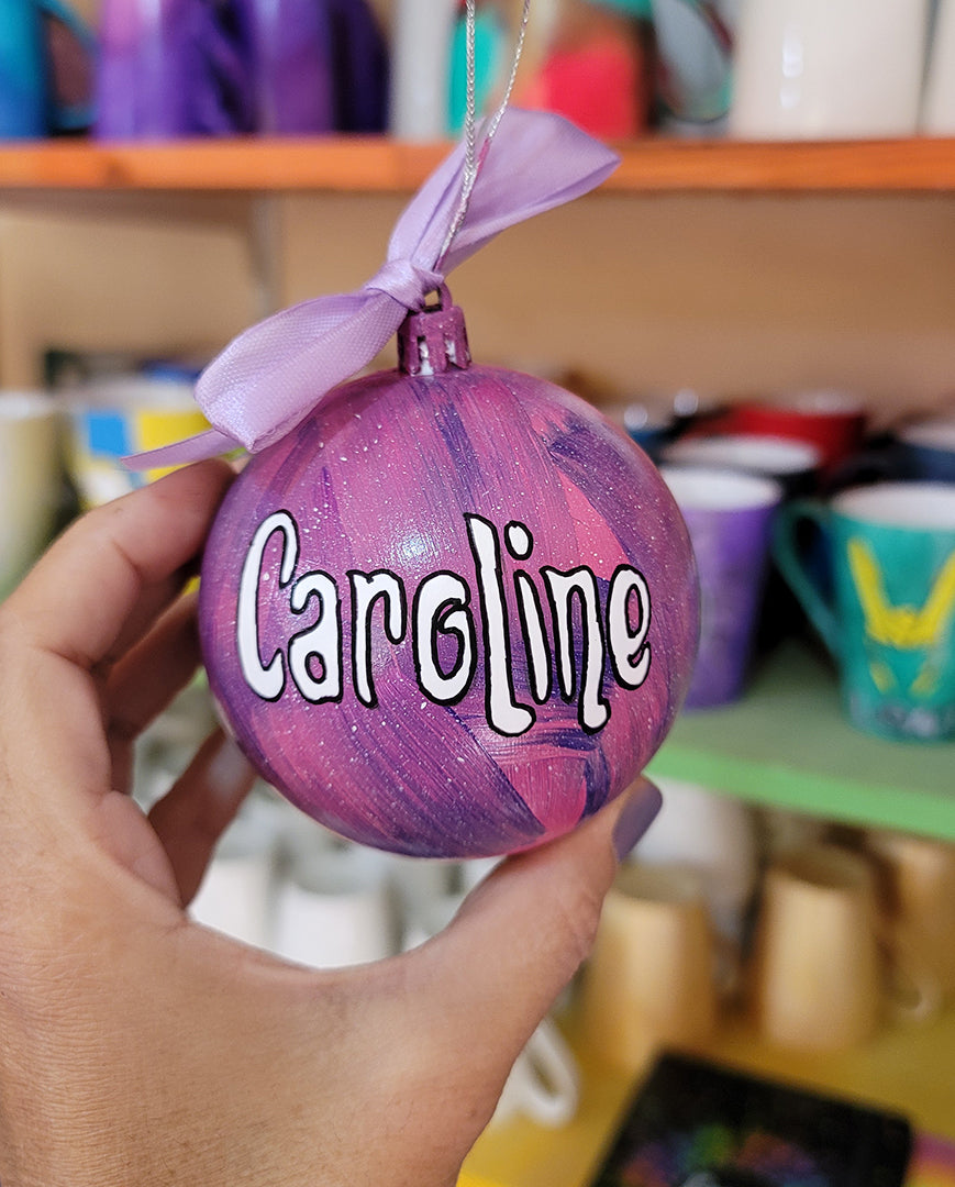 A Pink galaxy hand painted ornament with the name "Caroline" in white outlined with black