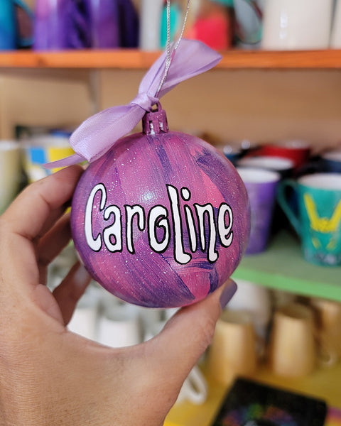 A Pink galaxy hand painted ornament with the name "Caroline" in white outlined with black