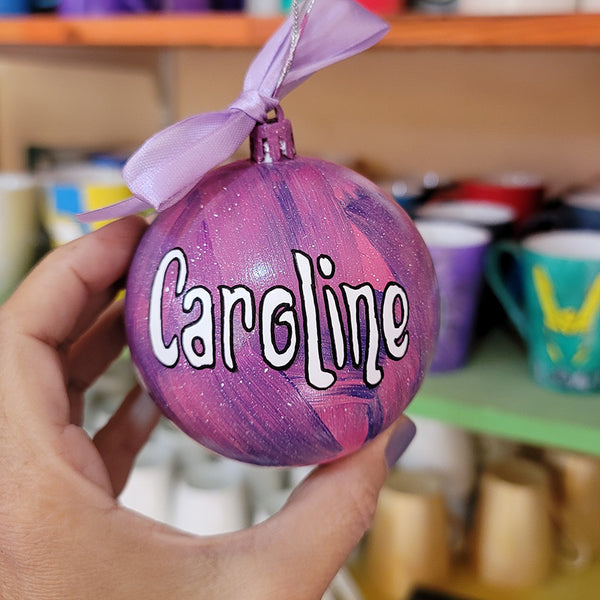 A Pink galaxy hand painted ornament with the name "Caroline" in white outlined with black