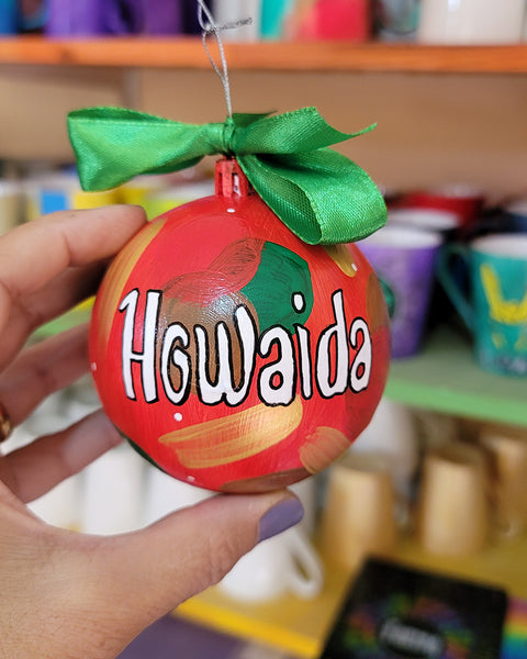 A Colorful hand painted ornament with red background and colors of red green, brown and gold scattered all over with white dots and the name "Howaida" written in white outlined with black