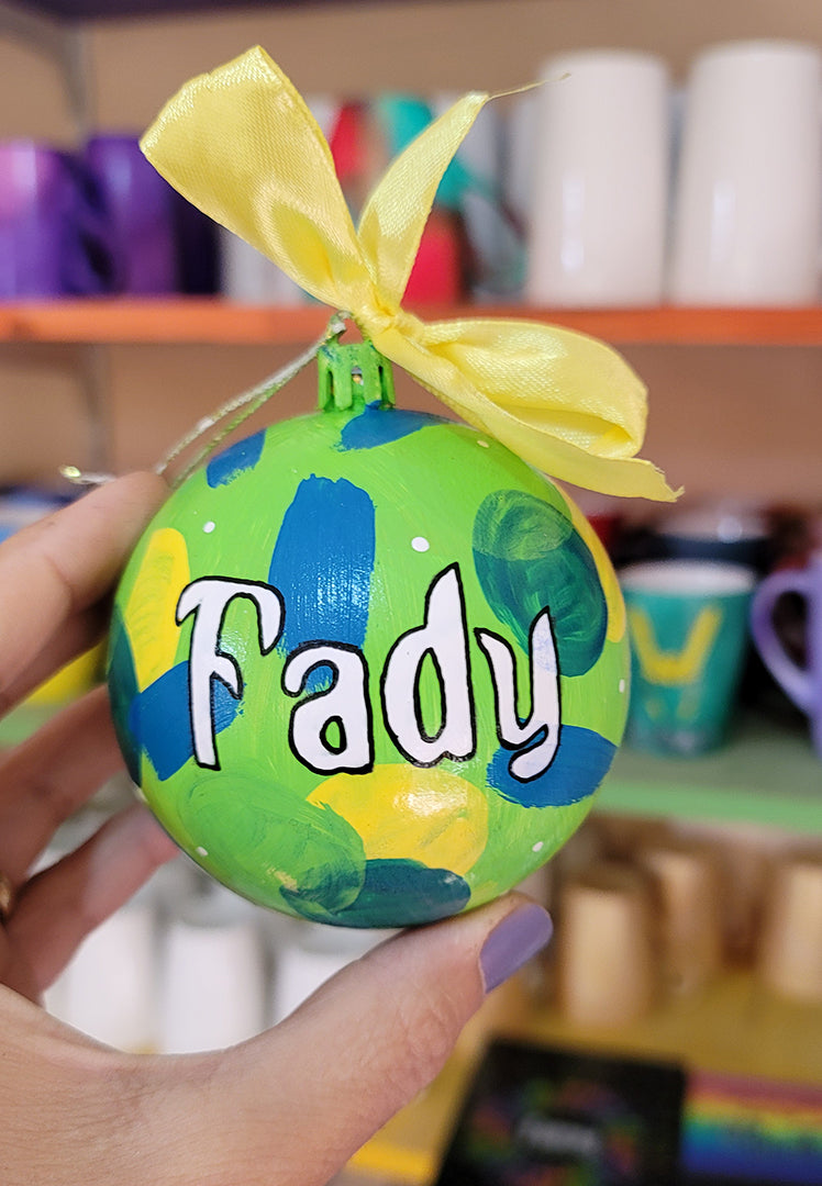 A Colorful hand painted ornament with lime green background and colors of lime green, teal, yellow and blue scattered all over with white dots and the name "Fady" written in white outlined with black