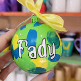 A Colorful hand painted ornament with lime green background and colors of lime green, teal, yellow and blue scattered all over with white dots and the name 