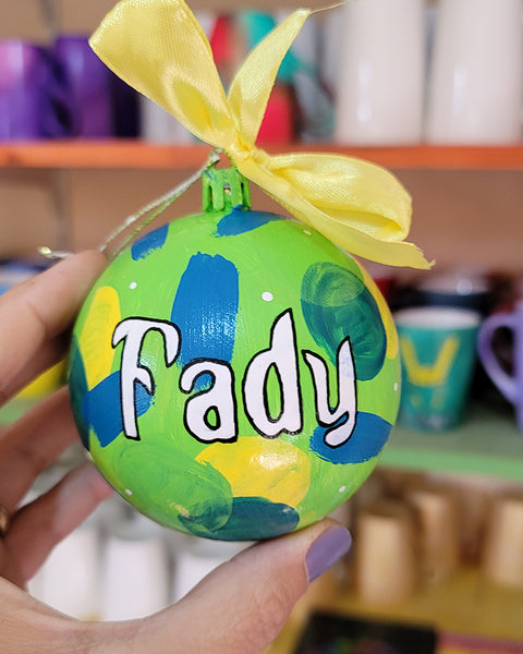 A Colorful hand painted ornament with lime green background and colors of lime green, teal, yellow and blue scattered all over with white dots and the name "Fady" written in white outlined with black