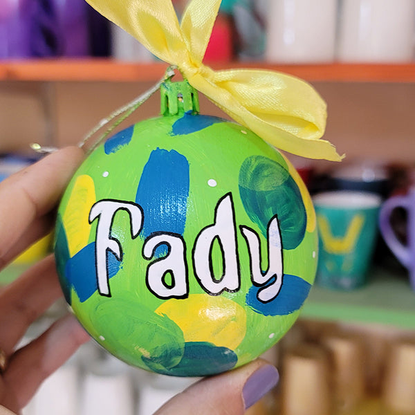 A Colorful hand painted ornament with lime green background and colors of lime green, teal, yellow and blue scattered all over with white dots and the name "Fady" written in white outlined with black