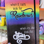 A notebook with the top half painted in rainbow and the bottom in dark galaxy, with the words on the rainbow written "when it rains look for rainbows" and the words on the galaxy written "when its dark look for stars"