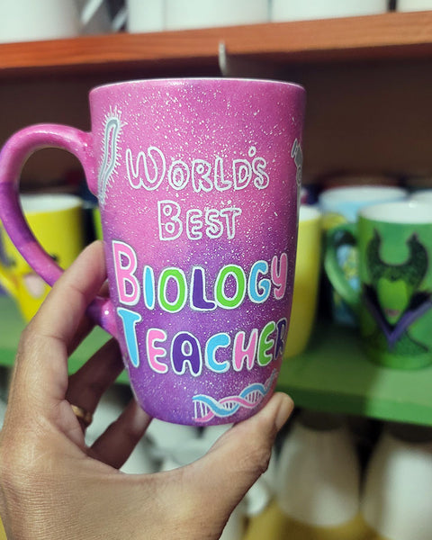 A Pink Galaxy hand painted mug with the words " worlds best biology teacher" and biology items scattered all over (DNA, Plant cell, microscope...etc.)