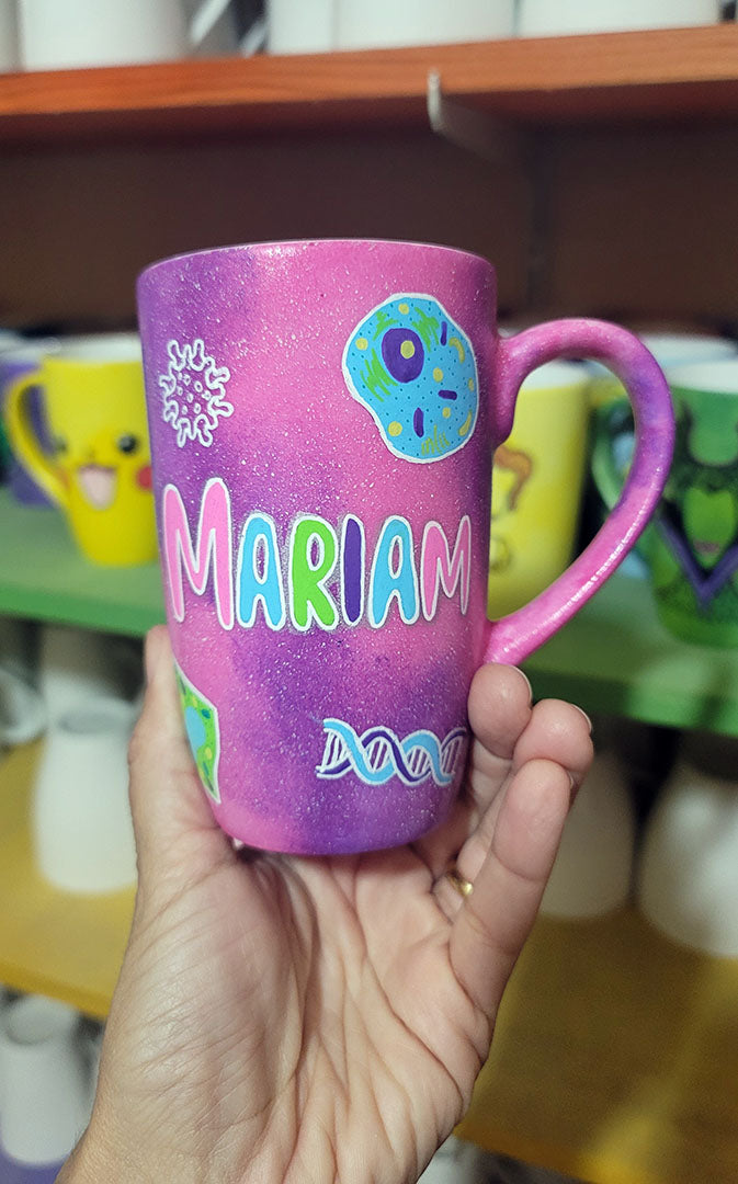 A Pink Galaxy hand painted mug with the name "Mariam" and biology items scattered all over (DNA, Plant cell, microscope...etc.)