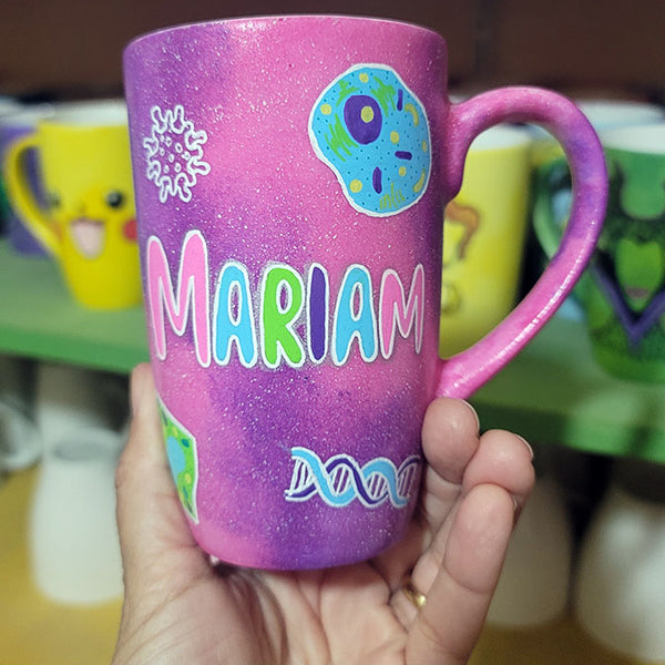 A Pink Galaxy hand painted mug with the name "Mariam" and biology items scattered all over (DNA, Plant cell, microscope...etc.)