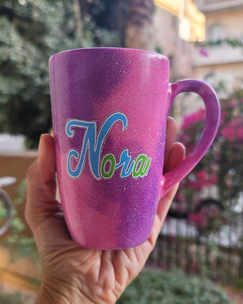 A hand painted pink galaxy mug with the name "Nora"