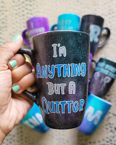 A Black galaxy hand painted mug with the sentence "I'm Anything but a quitter"