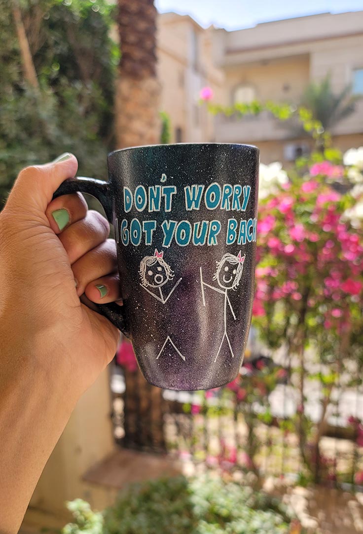 A hand painted black galaxy mug with the words "don't worry, I got your back " and a drawing of 2 stick figures with the girl holding the back of the other girl