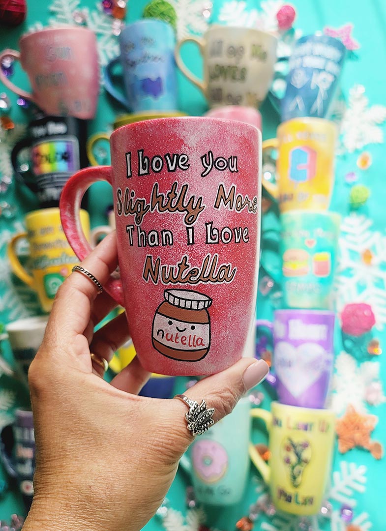 A red galaxy hand painted mug with the sentence "I love you slightly more than I love Nutella"and a small Nutella jar Painted with a smiley face