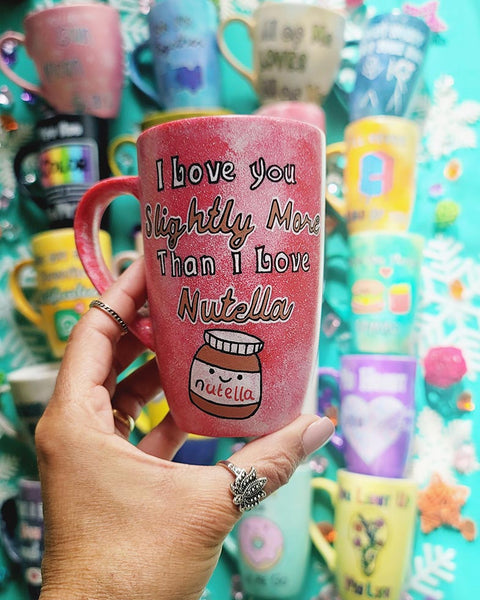 A red galaxy hand painted mug with the sentence "I love you slightly more than I love Nutella"and a small Nutella jar Painted with a smiley face