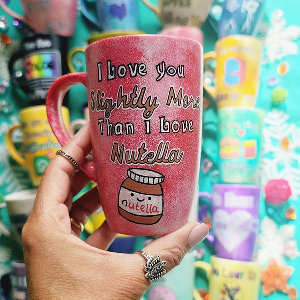 A red galaxy hand painted mug with the sentence "I love you slightly more than I love Nutella"and a small Nutella jar Painted with a smiley face