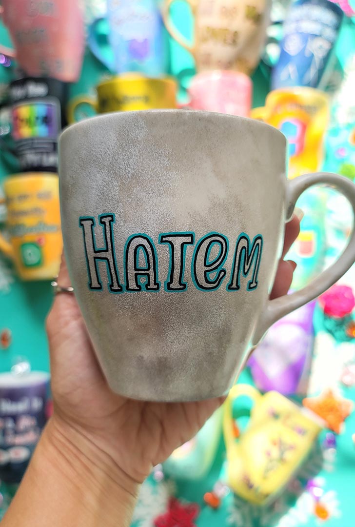 A hand-painted taupe silver mug with the name "Hatem"