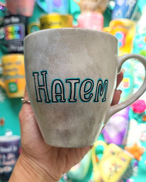 A hand-painted taupe silver mug with the name "Hatem"