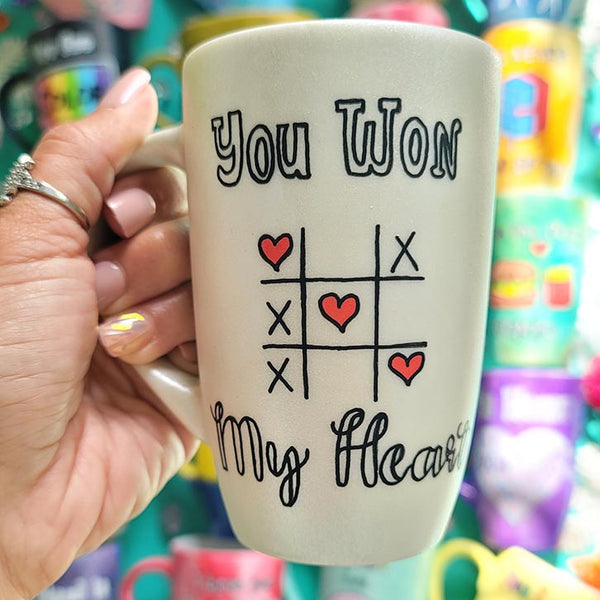 A hand painted pearl white mug with the sentence "you won" and under it an x o chart with hearts instead of o  and three hearts winning the game diagonally, then under it the words "My heart"