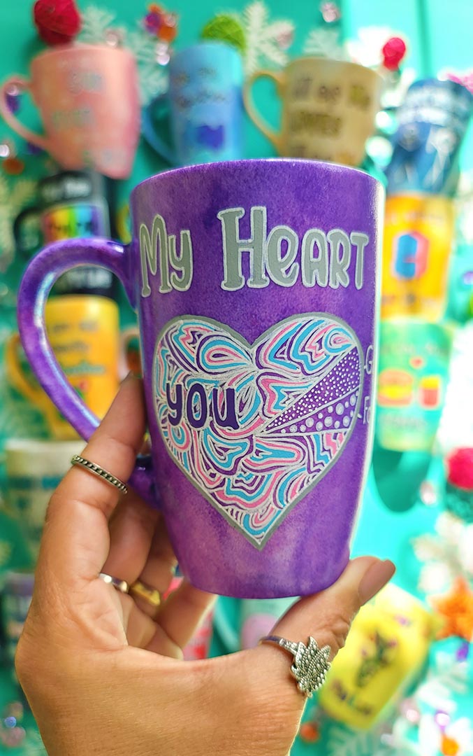 A Hand-Painted Purple galaxy mug with the words "My heart" and a large heart painted divided into a pie chart with a small part"gaming" and another small part"food" and most of the heart written inside it you