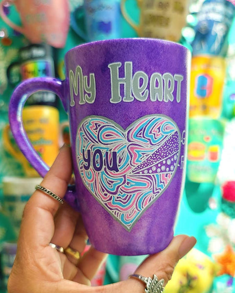 A Hand-Painted Purple galaxy mug with the words "My heart" and a large heart painted divided into a pie chart with a small part"gaming" and another small part"food" and most of the heart written inside it you