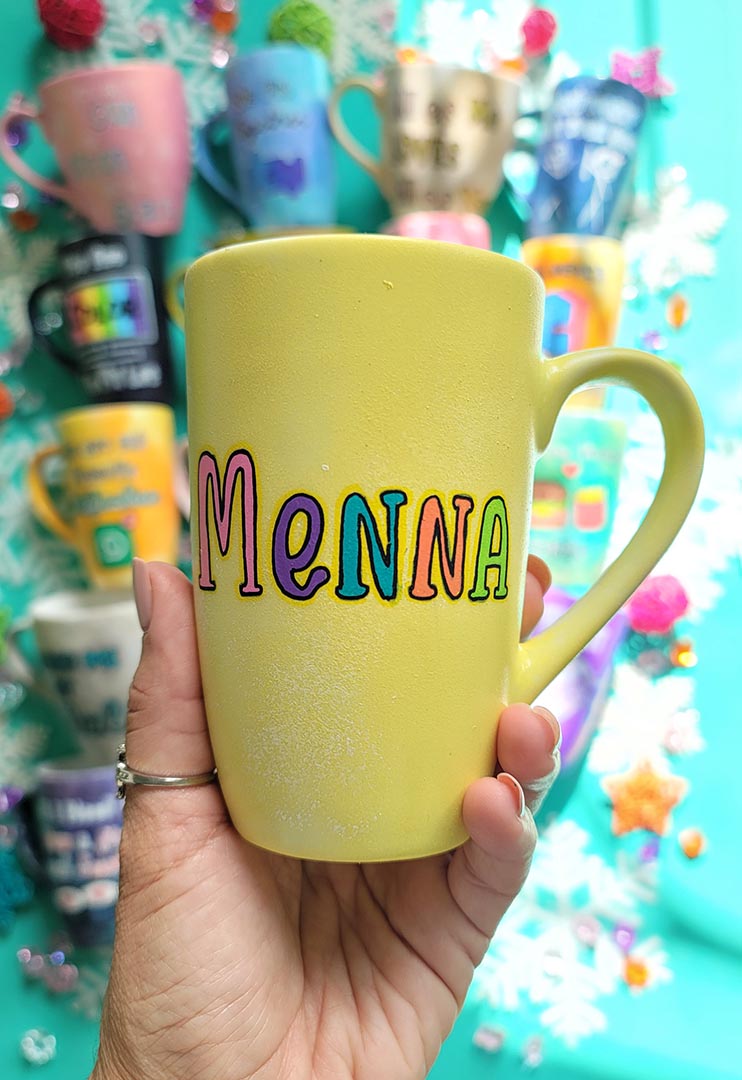 A Pastel yellow hand-painted mug with the name "Menna"