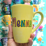 A Pastel yellow hand-painted mug with the name 