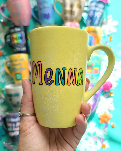 A Pastel yellow hand-painted mug with the name "Menna"