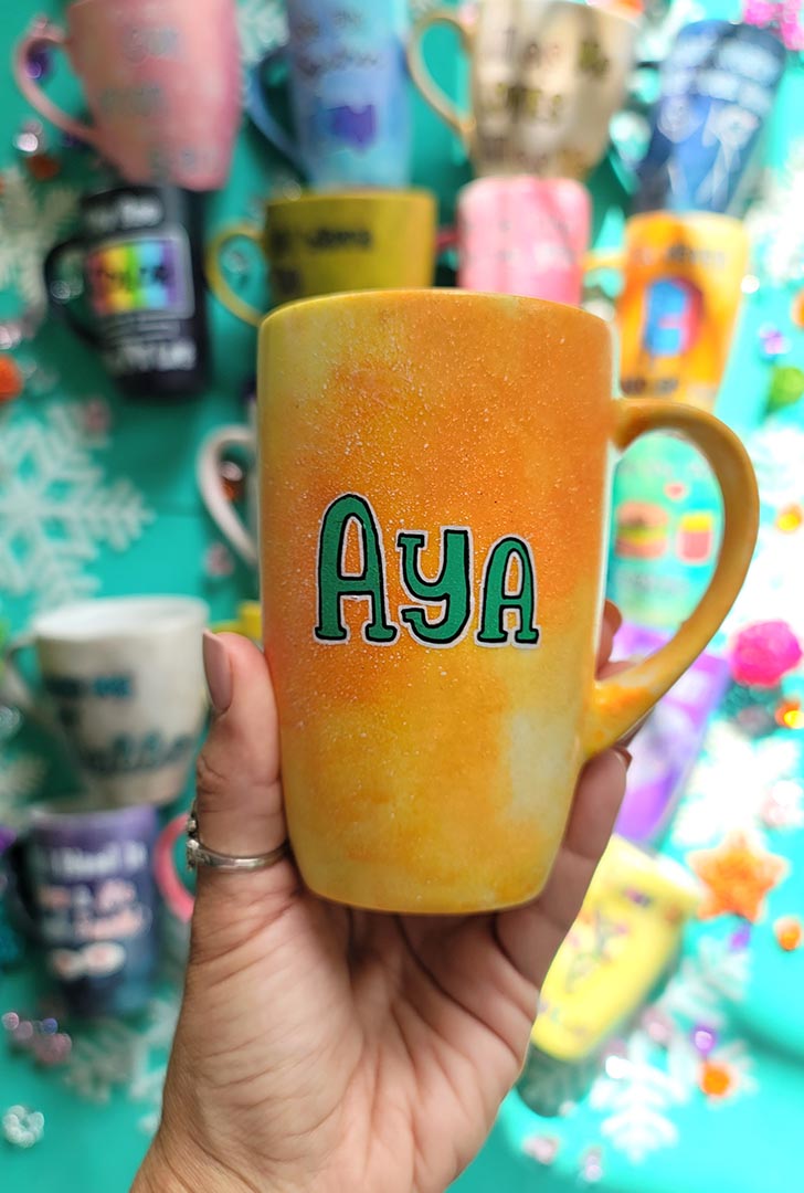 A yellow orange hand-painted mug with the name "Aya"