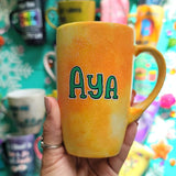 A yellow orange hand-painted mug with the name 