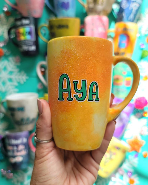 A yellow orange hand-painted mug with the name "Aya"