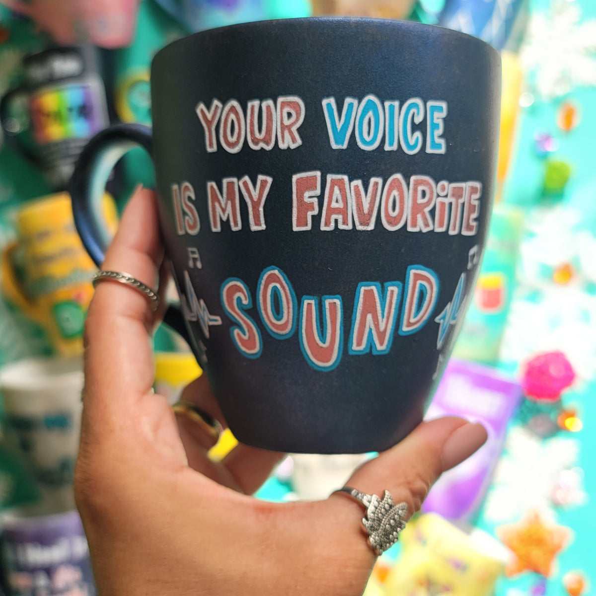 A shimmery blue hand painted mug with the sentence " your voice is my favorite sound" and sound beats painted on both sides