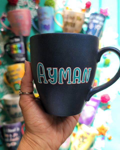 A shimmery blue hand painted mug with the name "Ayman"