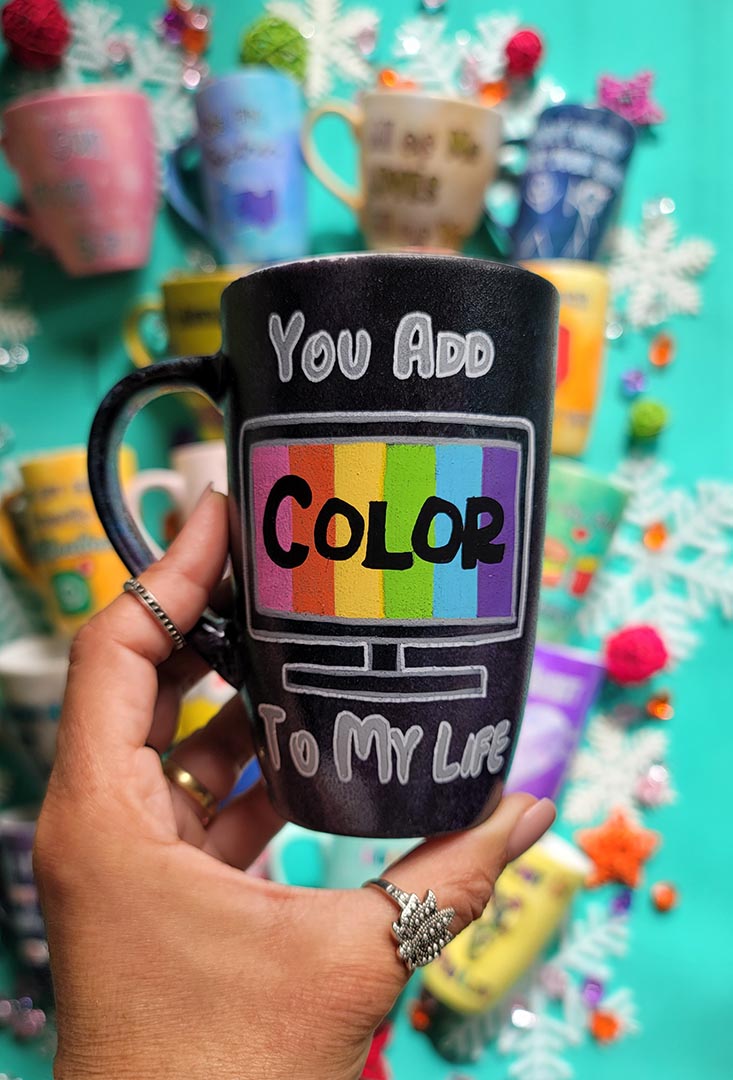 A hand-painted dark sky mug with the words "you add" on the top center, below it a tv led screen drawn with colors inside and the word "color" in black. then below it the words " to my life"