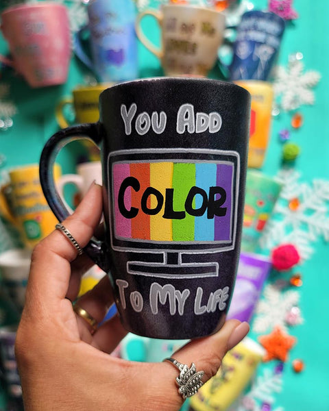 A hand-painted dark sky mug with the words "you add" on the top center, below it a tv led screen drawn with colors inside and the word "color" in black. then below it the words " to my life"