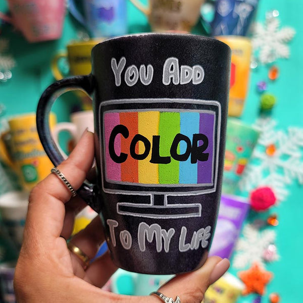 A hand-painted dark sky mug with the words "you add" on the top center, below it a tv led screen drawn with colors inside and the word "color" in black. then below it the words " to my life"