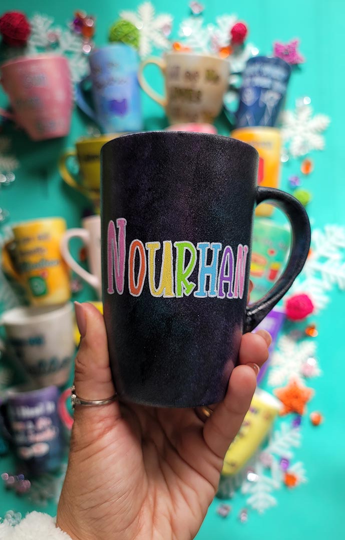 A hand-painted dark sky mug with the name "Nourhan"