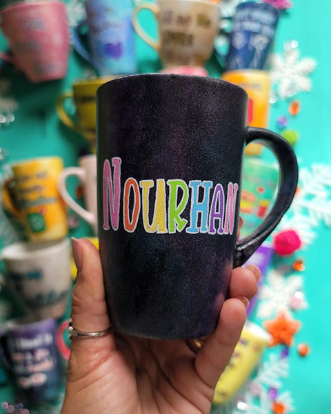 A hand-painted dark sky mug with the name "Nourhan"