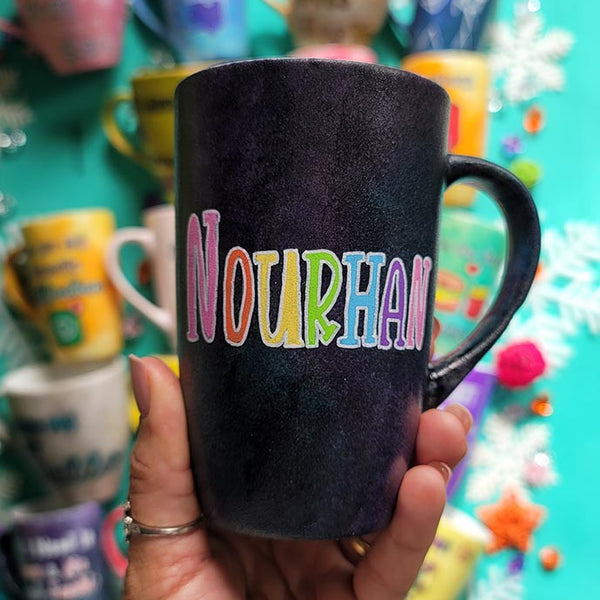 A hand-painted dark sky mug with the name "Nourhan"